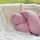 Die KraftKids GmbH Wickeltischrolle Musselin rosa, eine weiche, hellrosa Musselin-Wickelauflage, liegt auf einer flauschigen, cremefarbenen Decke auf einem weißen Kinderbett oder einer Bank mit einem verschwommenen grünen Hintergrund im Freien.