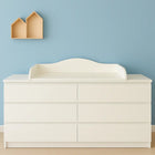 Ein weißer KraftKids Wickelaufsatz mit Blende für eine 160 cm breite MALM Kommode dient als Wickelstation vor einer hellblauen Wand. Zwei handgefertigte Regale in Hausform darüber betonen das minimalistische, saubere Design.