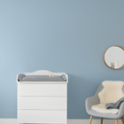 Ein KraftKids Wickelaufsatz weiß, passend für schmale 3er oder 4er Schubladen MALM Kommode, dient als praktische Wickelstation im Babyzimmer gegen eine hellblaue Wand. Daneben steht ein grauer Sessel mit weißem Fell und darüber ein runder Spiegel.