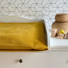 Eine weiße Kommode mit einer KraftKids Bezug für Wickeltischauflage Cord Breitcord in Gelb Senf und Holzklötzen darauf.