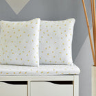 Zwei KraftKids Kissenbezug Musselin gelbe Zitronen ruhen auf einer passenden gepolsterten Bank mit Schubladen. Die Bank steht vor einer grauen Wand mit geometrischen Formen, und hoher Bambus in einer weißen Vase in der Nähe vervollständigt die Szene.