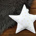 Ein weißes Sternkissen Musselin gelbe Zitronen von KraftKids mit kleinen gelben Aufdrucken liegt auf einem Holzboden neben einem flauschigen dunkelgrauen Teppich - ein niedlicher Akzent für jedes Kinderzimmer.