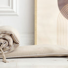 Die KraftKids Bettumrandung Nestchen Musselin beige, eine atmungsaktive Baumwoll-Bettumrandung mit Bindebändern und einem passenden Kissen, liegt auf einem hellen Holzboden neben einem gerahmten abstrakten Kunstwerk mit weichen geometrischen Formen.