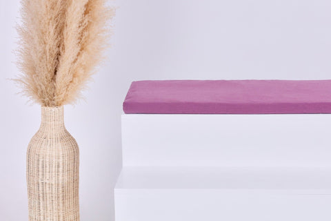 Eine hohe geflochtene Vase mit beigem Pampasgras steht neben weißen Stufen, die oberste Stufe wird von einer gefalteten KraftKids GmbH Sitzauflage für Ikea TROFAST Musselin purpur aus doppellagigem Musselin in zartem Lila gekrönt.