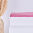 Eine hohe geflochtene Vase mit getrocknetem Pampasgras steht neben einer weißen stufenartigen Struktur, die mit der KraftKids GmbH Sitzauflage für Ikea TROFAST Cord Breitcord Rosa gekrönt ist, vor einem schlichten hellen Hintergrund.