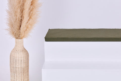 Eine hohe geflochtene Vase mit getrocknetem Pampasgras steht auf einem minimalistischen weißen Stufenpodest, das mit dem Kissen KraftKids GmbH Sitzauflage für Ikea TROFAST Doppelkrepp Grün Herbstgrün vor einem schlichten hellen Hintergrund versehen ist.