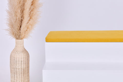 Eine hohe geflochtene Vase mit beigem Pampasgras steht neben einem weißen Stufenpodest, das mit der KraftKids GmbH Sitzauflage für Ikea TROFAST Doppelkrepp Gelb Senf vor einem schlichten hellen Hintergrund gekrönt wird.