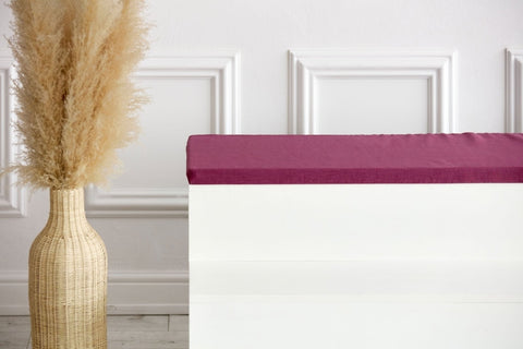 Eine große Korbvase mit Pampasgras steht neben einer weißen Bank mit der KraftKids GmbH Sitzauflage für Ikea TROFAST Leinen magenta dunkel, vor einer weißen Wand mit Zierleiste.