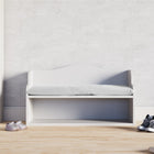 Die KraftKids Kindersitzbank weiß mit Sitzauflage steht vor einer strukturierten weißen Wand, daneben Sneakers auf Holzboden - ein gemütlicher Look für jedes Kinderzimmer mit praktischer Sitzbank und Stauraum.