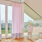 Ein helles Zimmer mit großen Fenstern, Holzboden und einer leichten Holzwiege am Fenster. KraftKids Gardinen Unigrau weiße Punkte auf Rosa verleihen dem Babyzimmer eine charmante Note - ideal für die Einrichtung mit Blick ins Grüne.