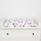 Der KraftKids Wickelaufsatz für HEMNES & IDANÄS schmal wird auf einem weißen Wickeltisch mit schwarzen Knöpfen und einer bunten gepolsterten Matte mit roten, blauen und weißen Strandhütten und Leuchttürmen gezeigt. Der Hintergrund ist einfarbig weiß.