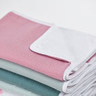 Ein ordentlich gefalteter Stapel von KraftKids Wickelunterlage Musselin rosa Babydecken in rosa, weiß, grün und gemustert, plus eine wasserundurchlässige Unterlage für zusätzlichen Schutz, angeordnet auf einem schlichten weißen Hintergrund.