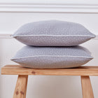 Zwei KraftKids Kissenbezug Musselin grau Punkte mit kleinen weißen Punkten sind auf einem Holzhocker vor einer weißen Wand gestapelt - eine ideale Ergänzung für Ihre Bettwäschesammlung.