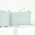 Ein grünes rechteckiges KraftKids Bettumrandung Nestchen mit goldenen Sprenkeln, hergestellt aus weichem Musselin, wird auf weißen geometrischen Blöcken vor einem weißen Hintergrund dargestellt.