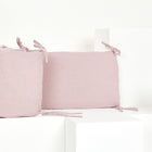 Zwei blassrosa Bettumrandung Nestchen Musselin goldene Punkte auf Rosa von KraftKids, mit 100% Baumwolle Stoff und gebundenen Ecken, werden auf weißen geometrischen Blöcken vor einem weißen Hintergrund dargestellt.