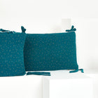 Die KraftKids Bettumrandung Nestchen Musselin in Petrol mit goldenen Punkten ruht auf gestaffelten weißen geometrischen Plattformen vor einem schlichten weißen Hintergrund.