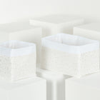 Zwei KraftKids Körbchen Musselin goldene Punkte auf Weiß sind auf weißen Blöcken abgebildet. Diese beigefarbenen Stoffkörbchen mit weißer Innenseite und goldenen Punkten in zwei Größen sind perfekt für die Organisation Ihres Wickeltisches.