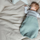 Auf beigem Bettzeug schläft ein Baby mit Schnuller, das ein weißes Hemd und den KraftKids Strampelsack Frühling Sommer Musselin mint trägt; neben dem Baby liegen sternförmige Kissen.