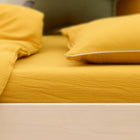 Eine Nahaufnahme eines ordentlich gemachten Bettes mit dem KraftKids Spannbettlaken Doppelkrepp Gelb Senf, mit passendem gelben Kissen und Decke auf einem hellen Holzrahmen vor einem sanft verschwommenen Hintergrund.