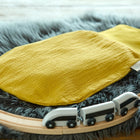 Ein KraftKids Strampelsack Herbst Winter Doppelkrepp Gelb Senf liegt auf einem grauen Kunstfellteppich neben einem Baby Fusssack, umgeben von einer hölzernen Spielzeugeisenbahnstrecke mit einem schwarz-weißen Zug.
