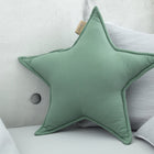 Ein Sternkissen Doppelkrepp Grün Jade von KraftKids, sternförmig und grün, ruht vor hellgrauen Kissen und einer Betonwand und verleiht jedem Kinderzimmer einen gemütlichen, modernen Touch.