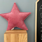 Das KraftKids Sternkissen Cord Breitcord Rosa sitzt auf einem Holzquader vor grauer Wand. Daneben zeigt eine Tafel handgezeichnete Buchstaben A-E in Weiß - ein liebevoller Akzent fürs Kinderzimmer.