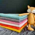 Ein Stapel von sieben bunten, gefalteten Cordstoffen, darunter die KraftKids Wickelunterlage Cord Breitcord Mint, ruht auf einer grauen, pelzigen Oberfläche neben einem weichen, orangefarbenen Fuchsplüsch - perfekt als Wickelunterlage Baby oder reisewickelunterlage.