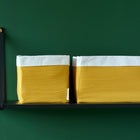 Zwei Körbchen Doppelkrepp Gelb Mustard von KraftKids mit weißen Rändern stehen auf einem schwarzen, wandmontierten Regal vor einer dunkelgrünen Wand - die perfekte Aufbewahrung am Wickeltisch.