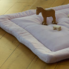 Die KraftKids Krabbeldecke Doppelkrepp Rosa in zartem Rosa liegt auf einem Holzboden, auf dem Holzklötze und ein Spielzeugpferd platziert sind, und schafft eine einladende und warme Atmosphäre.