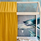 A Bettbaldachin Doppelkrepp Gelb Mustard von KraftKids sorgt vor einer blauen Wal-Malerei für Farbakzente. Decken auf der Matratze machen das Musselin Kinderzimmer besonders gemütlich.