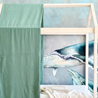 Ein KraftKids Bettbaldachin Doppelkrepp in Grün Jade hängt vor einer Wandmalerei mit blauen Walen, während eine beigefarbene Decke für Gemütlichkeit sorgt - die perfekte Kinderzimmer Deko für fantasievolles Spielen und erholsame Nächte.